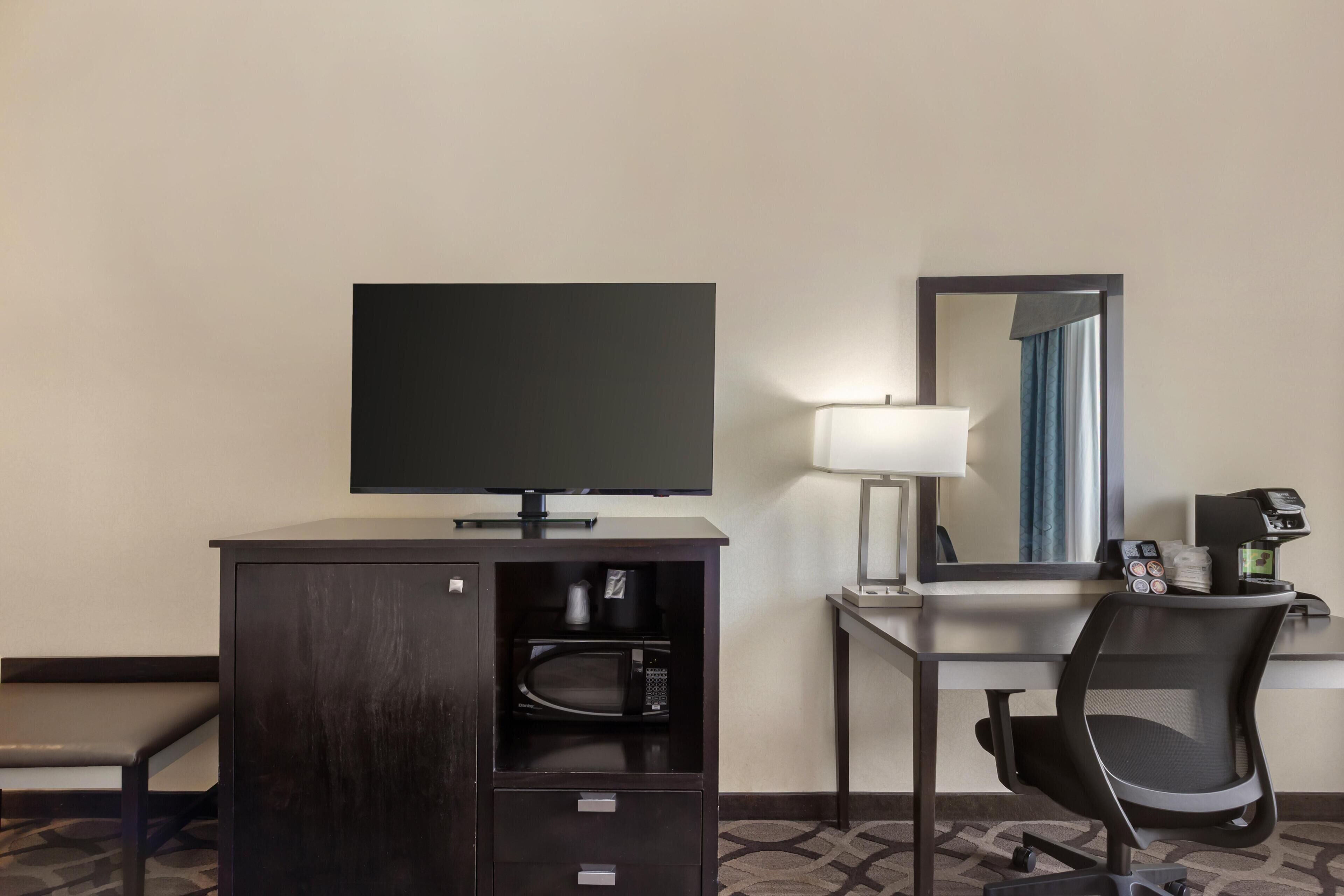 Ett hotellrum med ett skrivbord, en stol, en tv, en lampa och en kaffemaskin.