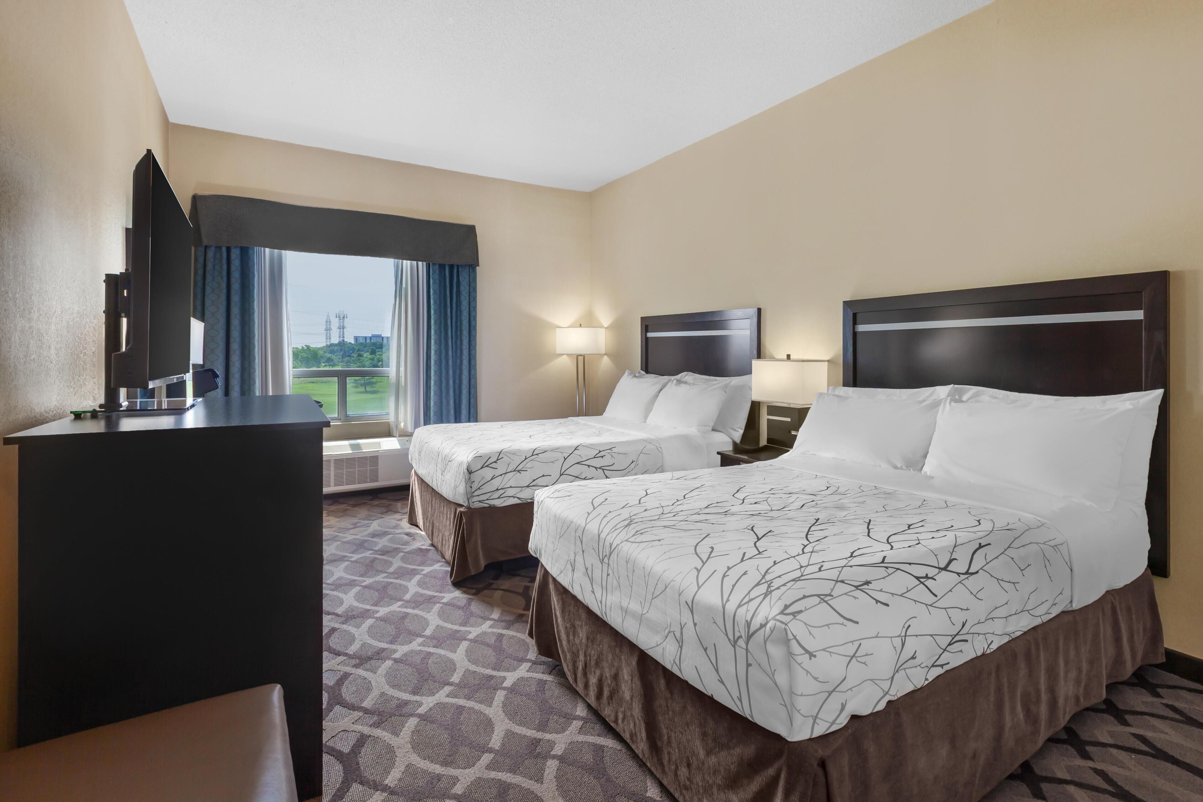 A hotel room with two beds, a desk, a chair, a window with curtains, and a view of the outdoors.