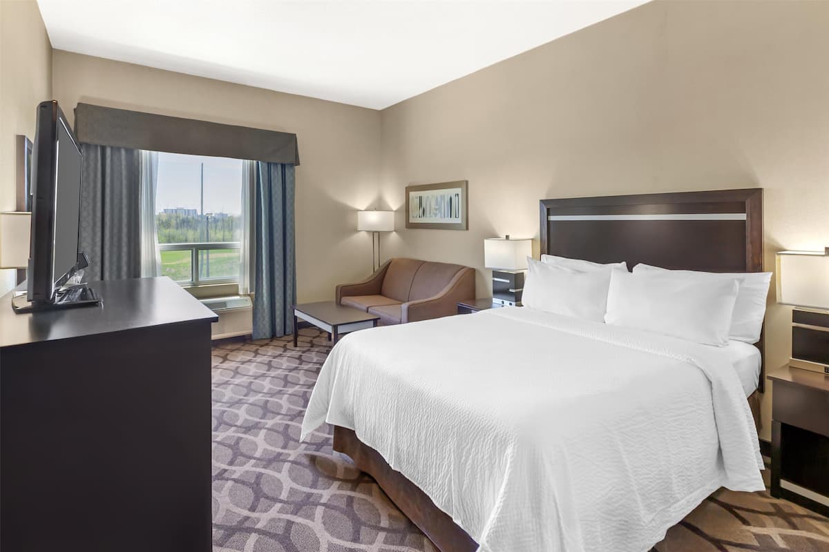 Una habitación de hotel con una cama grande, un escritorio, una silla, una lámpara y un ventanal con cortinas.