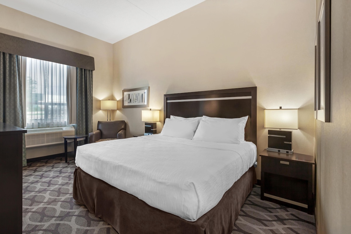 A hotel room with a large bed, a desk, a chair, two bedside tables with lamps, and a window with curtains.
