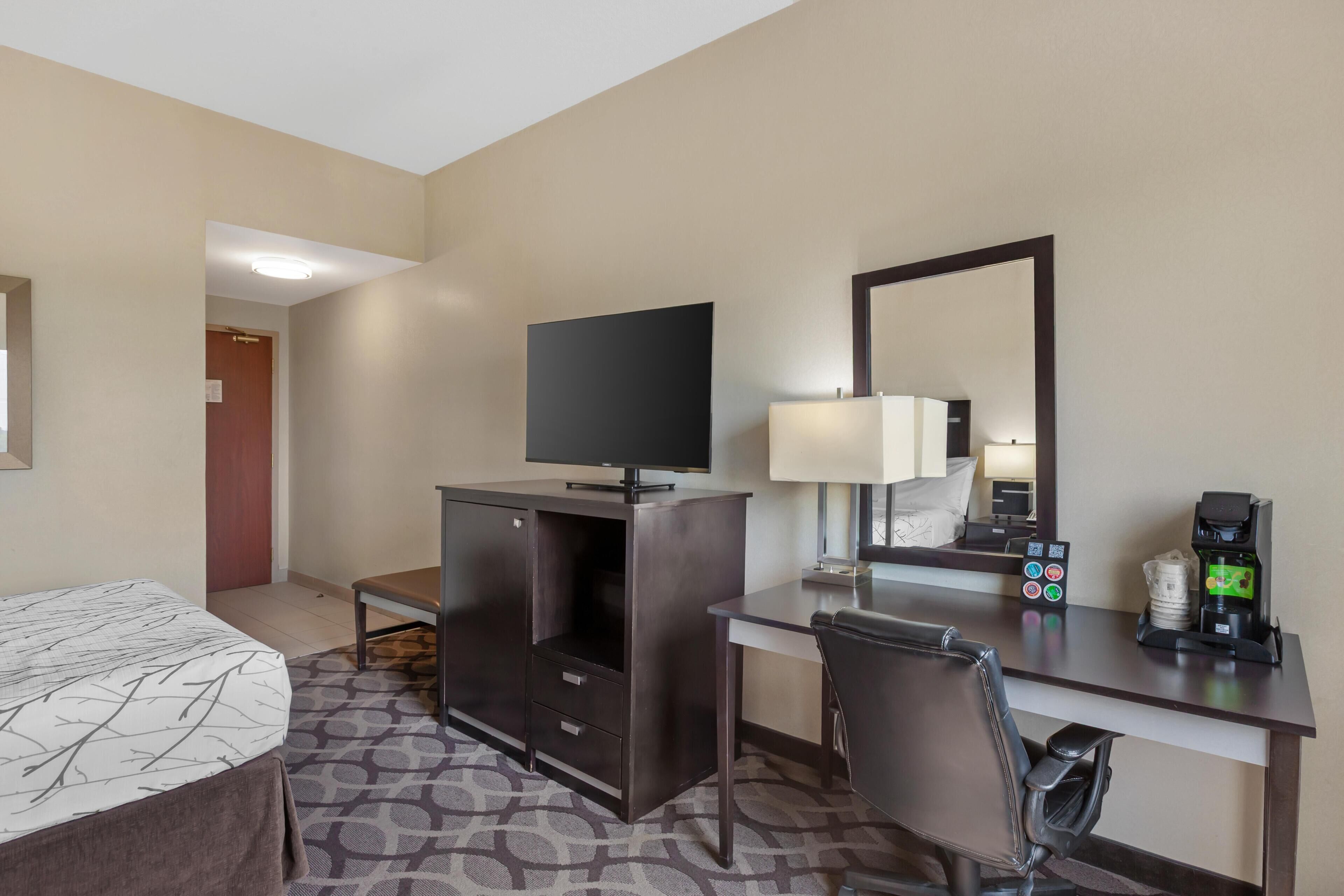 Une chambre d’hôtel comprenant un lit, un bureau avec une chaise, une télévision, une machine à café et un miroir.