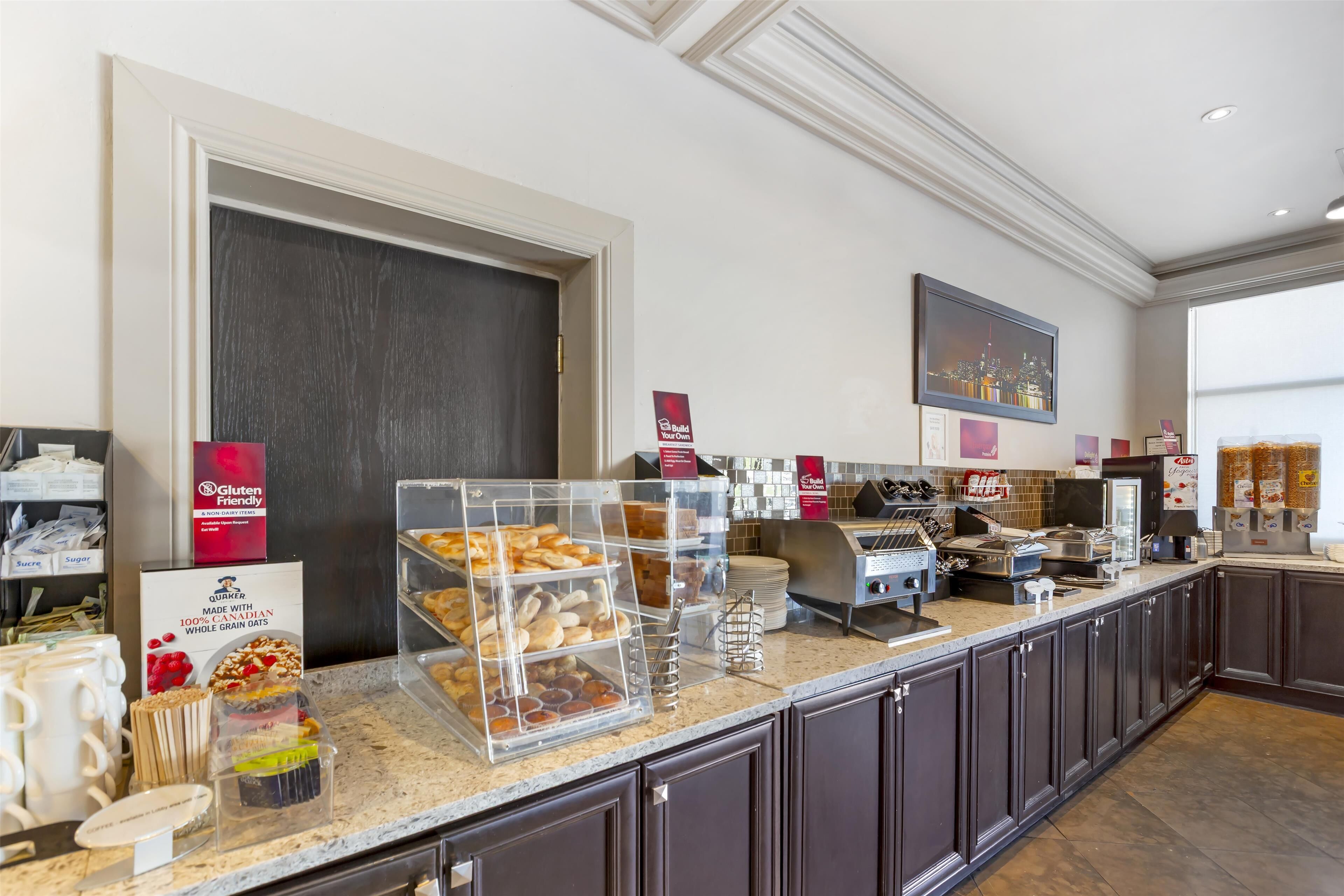 A hotel breakfast area with a self-serve station, gluten-free options, and a cityscape view.