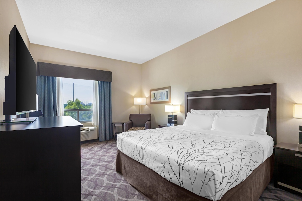 A hotel room with a large bed, a desk, a chair, a TV, and a window with curtains.