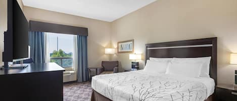 A hotel room with a large bed, a desk, a chair, a TV, and a window with curtains.