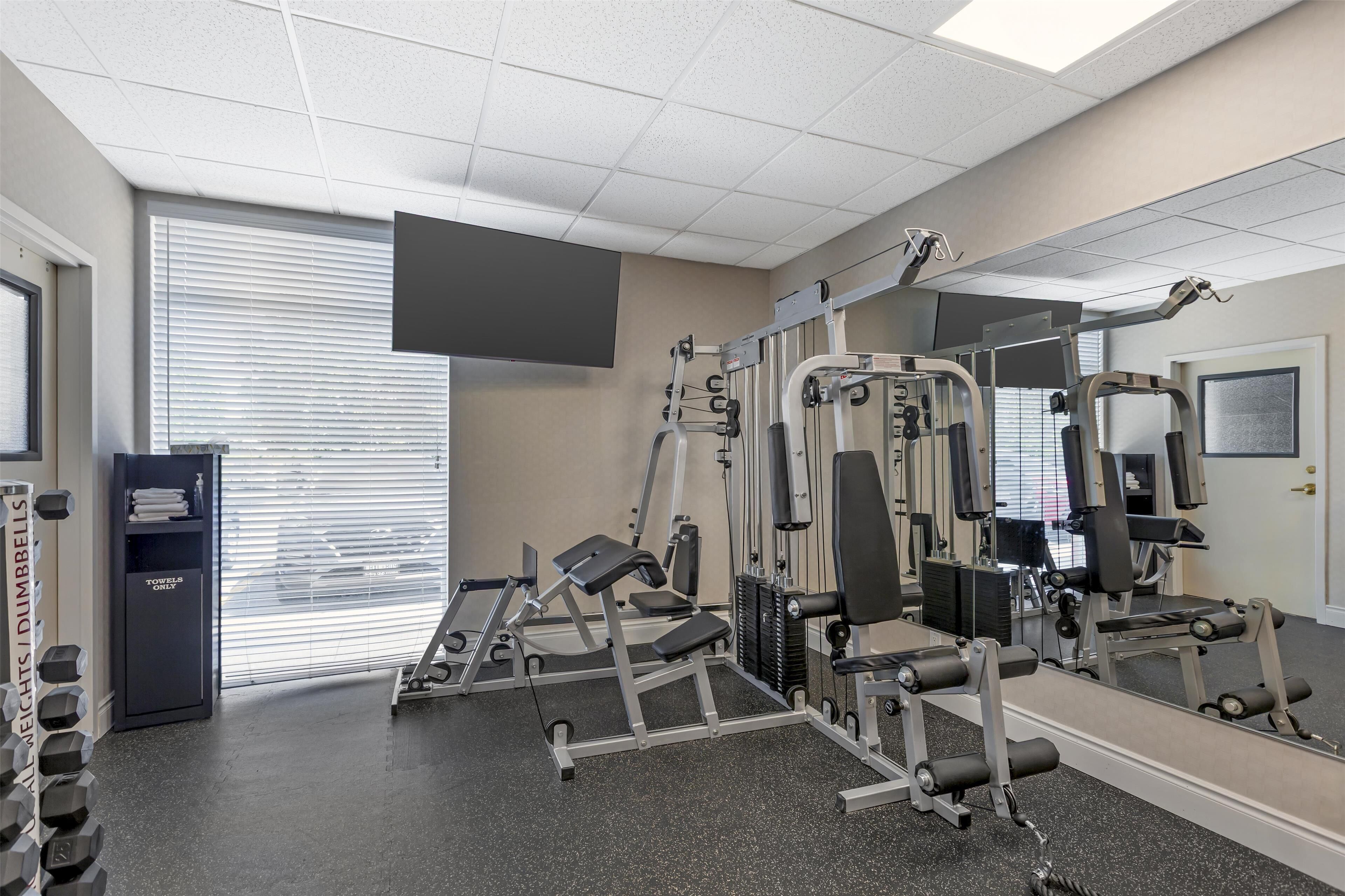 A gym with weight machines, a mirror, and a TV on the wall.