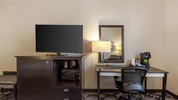 A hotel room with a bed, a desk with a chair, a television, a microwave, a coffee machine, and a mirror.
