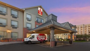 A hotel with a covered entrance, a van with 'BW' branding, and a sign indicating 'Best Western Plus' amenities.