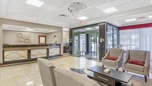 A hotel lobby with a reception desk, seating area, and a glass door entrance.