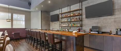 A bar area with a long counter, multiple stools, and a wall-mounted TV.