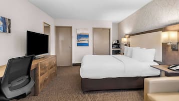 A hotel room with a bed, a desk with a computer, a television, and a coffee machine.