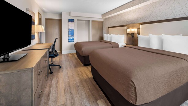 Ett hotellrum med en platt-TV, ett skrivbord med en stol, två sängar med bruna sängkläder, en garderob och en väggmonterad lampa.