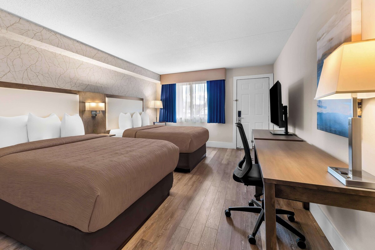Habitación de hotel con dos camas, un escritorio, un televisor y una ventana con cortinas.
