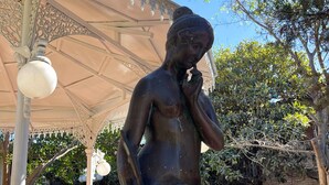 En staty av en kvinna i en park, med en lusthus i bakgrunden.