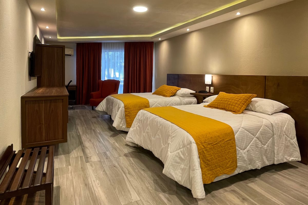 Una habitación de hotel con dos camas, suelo de madera, un escritorio, una silla y un televisor.