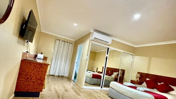 A hotel room with a wooden table, a bed with red pillows, an air conditioning unit, and a television on the wall. - Townview Motel (Townview)