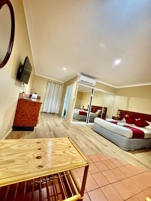 A hotel room with a wooden table, a bed with red pillows, an air conditioning unit, and a television on the wall. - Townview Motel (Townview)