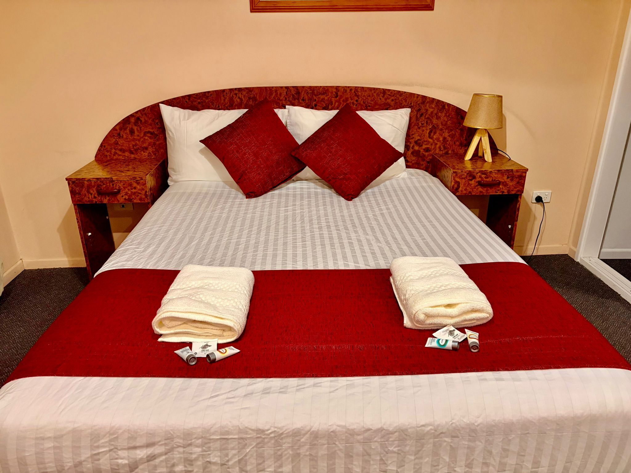 A neatly made bed with a red bedspread, two pillows, and two folded towels on the bed.