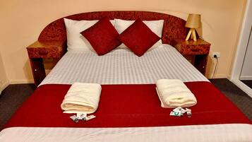 A neatly made bed with a red bedspread, two pillows, and two folded towels on the bed.