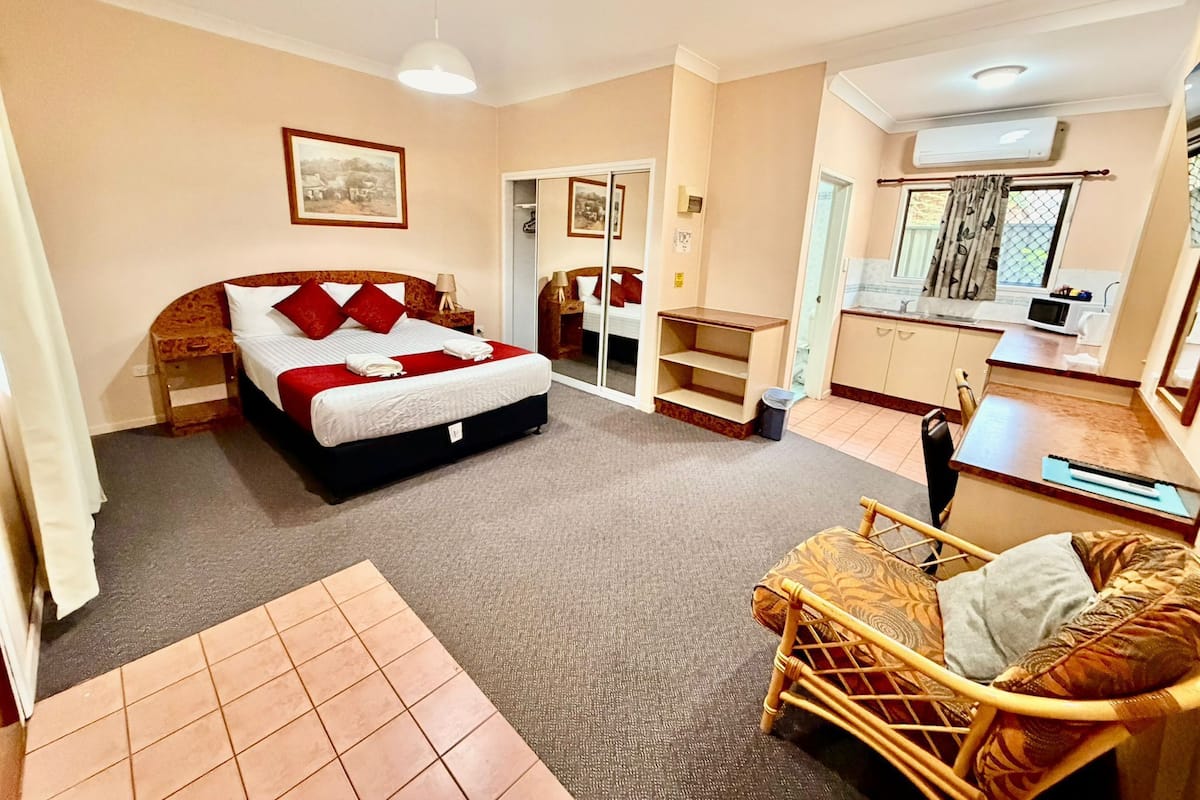 Une chambre d’hôtel comprenant un lit, un petit coin salon, une kitchenette et une salle de bain visible à travers une porte ouverte.