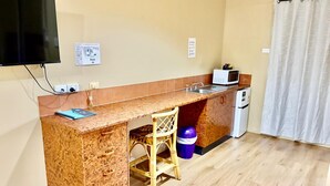 A compact kitchen with a wooden countertop, a microwave, a sink, and a small refrigerator. There are two stools and a trash bin. - Townview Motel (Townview)