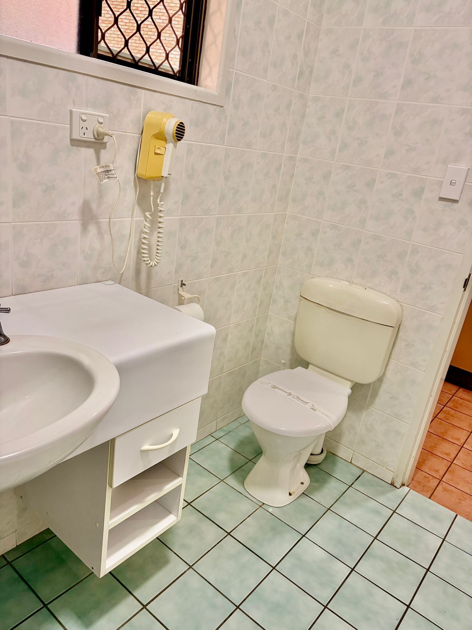 Un baño con un lavamanos blanco, un inodoro y un secador de pelo montado en la pared.