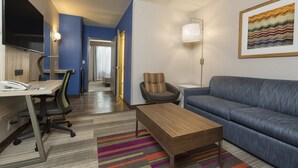 A modern hotel room with a desk, office chair, sofa, and a colorful striped rug. - Holiday Inn Express & Suites S Lake Buena Vista by IHG (Kissimmee)