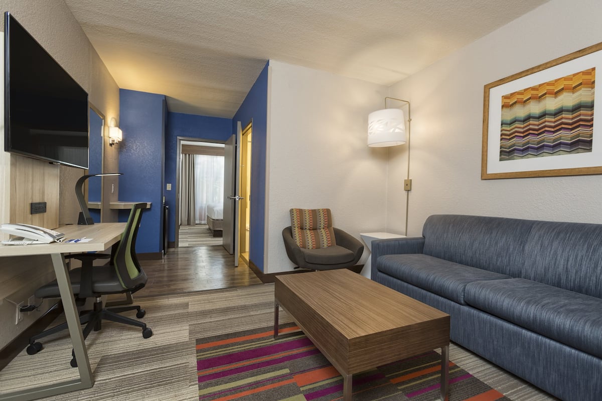 A modern hotel room with a desk, office chair, sofa, and a colorful striped rug.