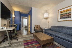 A modern hotel room with a desk, office chair, sofa, and a colorful striped rug. - Holiday Inn Express & Suites S Lake Buena Vista by IHG (Kissimmee)