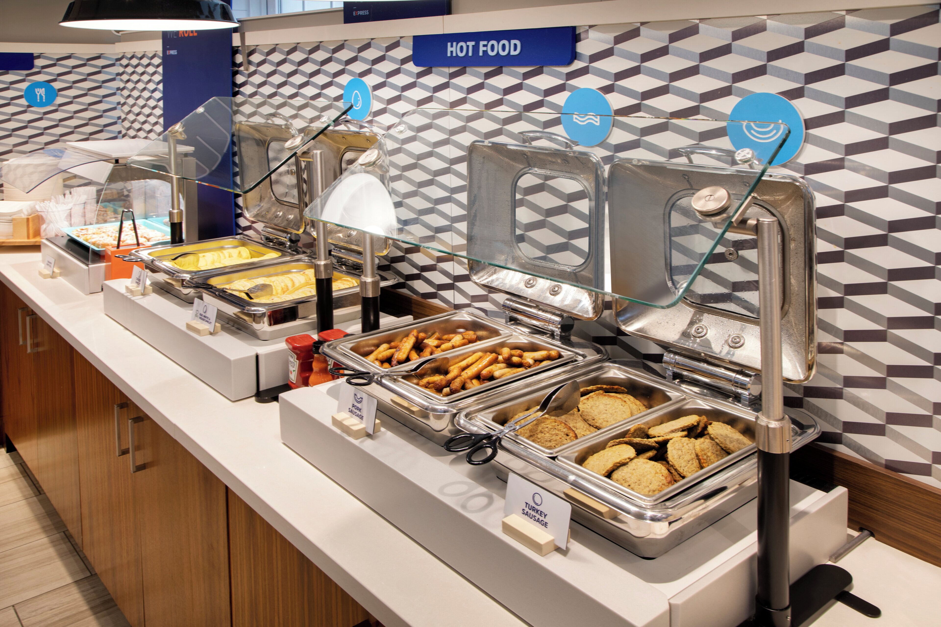 Un buffet proposant différents plats, chacun clairement identifié, notamment des saucisses de dinde, des saucisses de porc et des plats chauds.