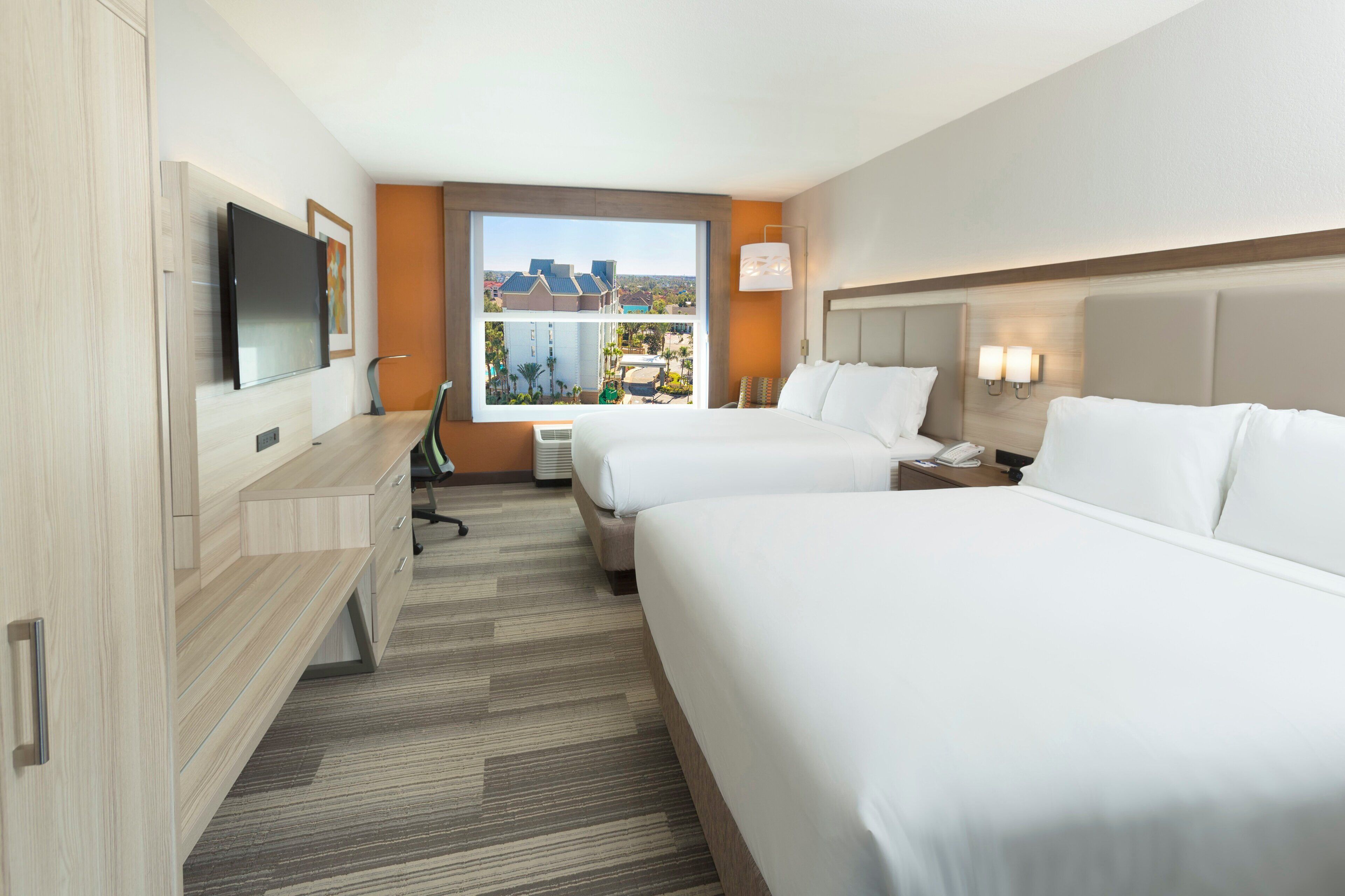 Une chambre d’hôtel avec deux lits, un bureau, une chaise, une télévision et une fenêtre donnant sur la ville.