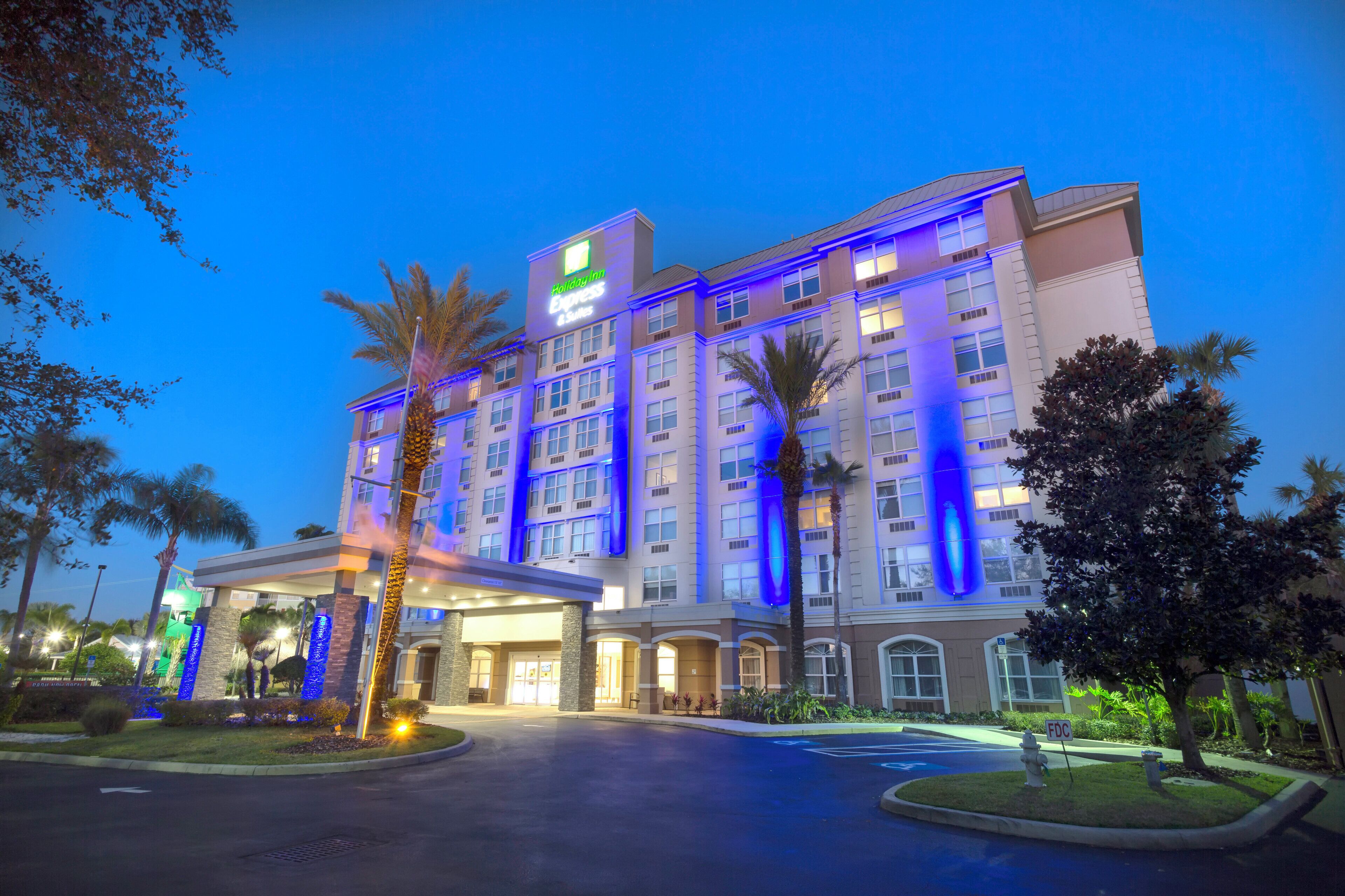 Un hotel de varios pisos con un llamativo letrero de Holiday Inn Express, una entrada cubierta y palmeras.