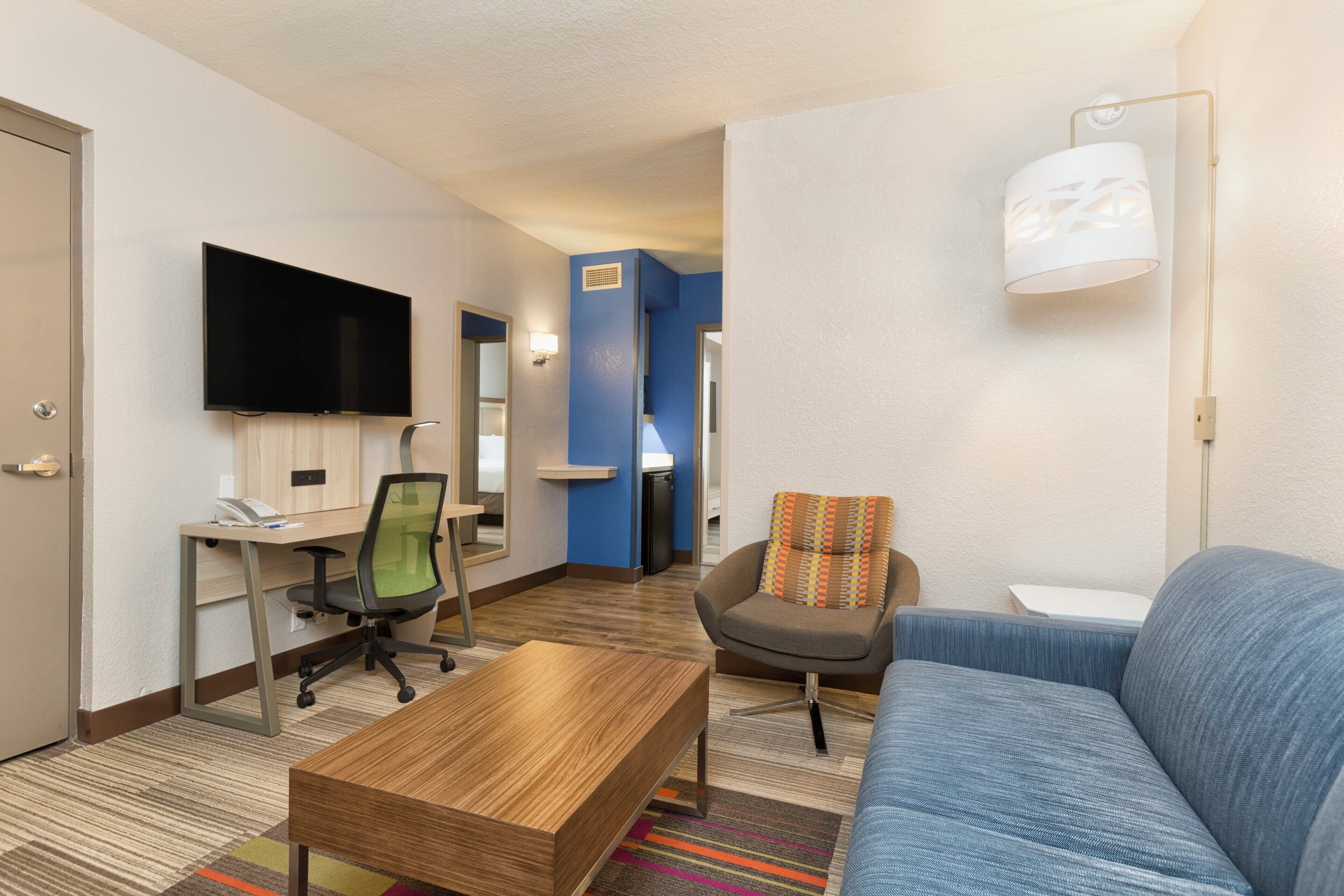 Ein Hotelzimmer mit Flachbildfernseher, Schreibtisch mit Computer, Sofa, Couchtisch und Lampe.