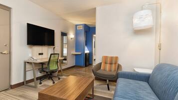 Ein Hotelzimmer mit Flachbildfernseher, Schreibtisch mit Computer, Sofa, Couchtisch und Lampe.