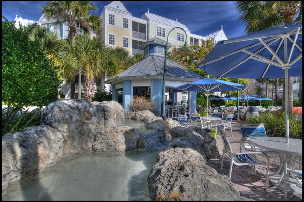 A resort pool area with a small gazebo, lounge chairs, and umbrellas. - Holiday Inn Express & Suites S Lake Buena Vista by IHG (Kissimmee)
