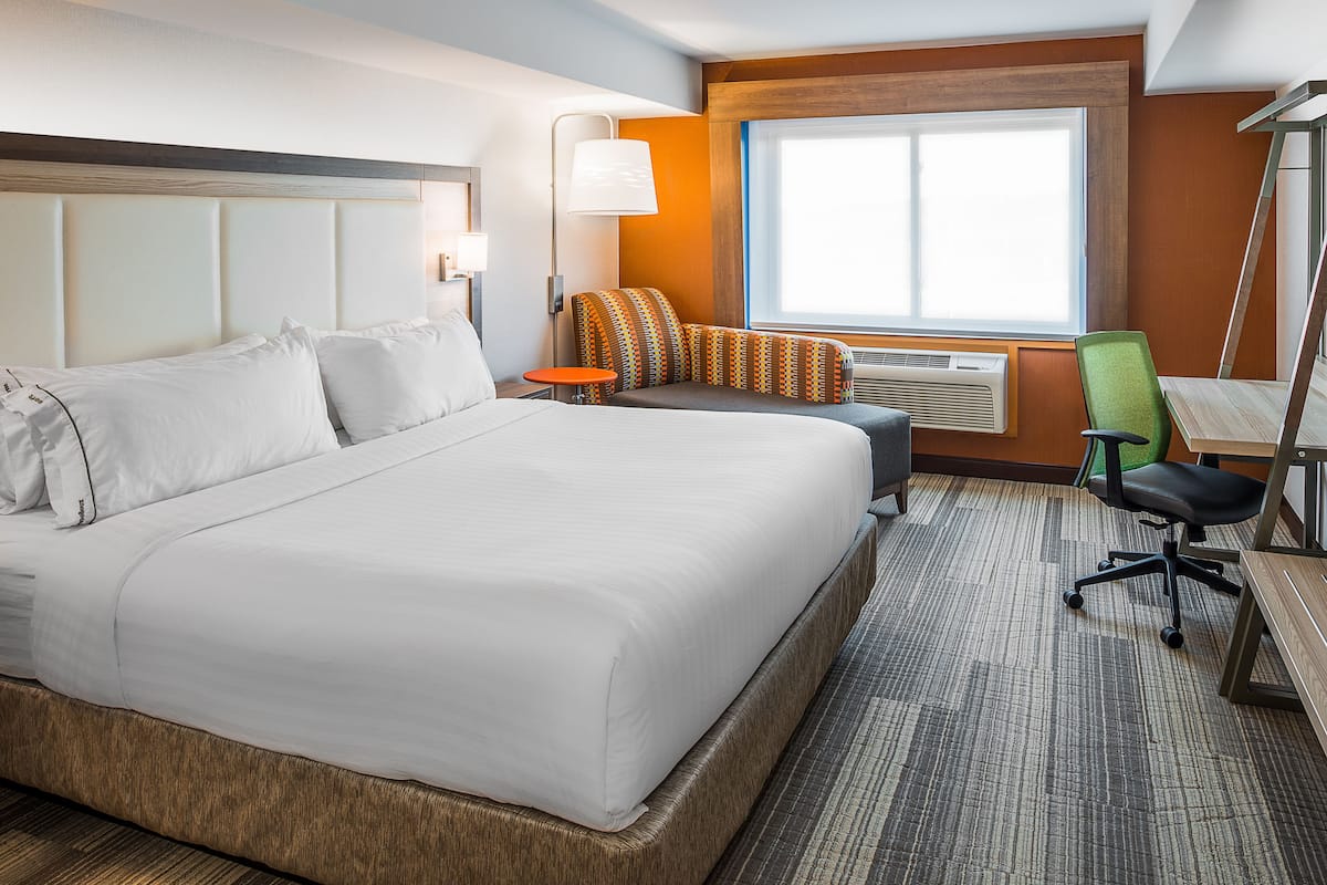 A hotel room with a large bed, a small table, a chair, and a window with a view.