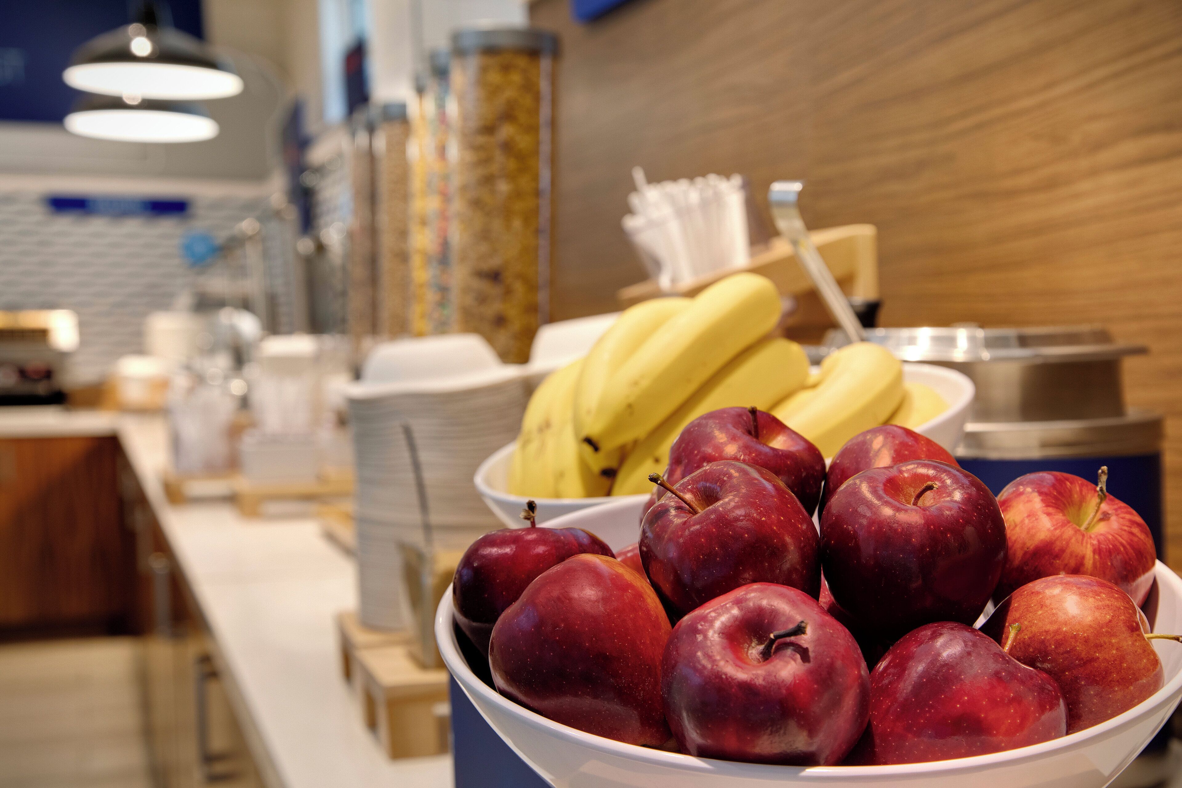 Un bol de manzanas rojas y un plato de plátanos en una zona de exhibición de alimentos.