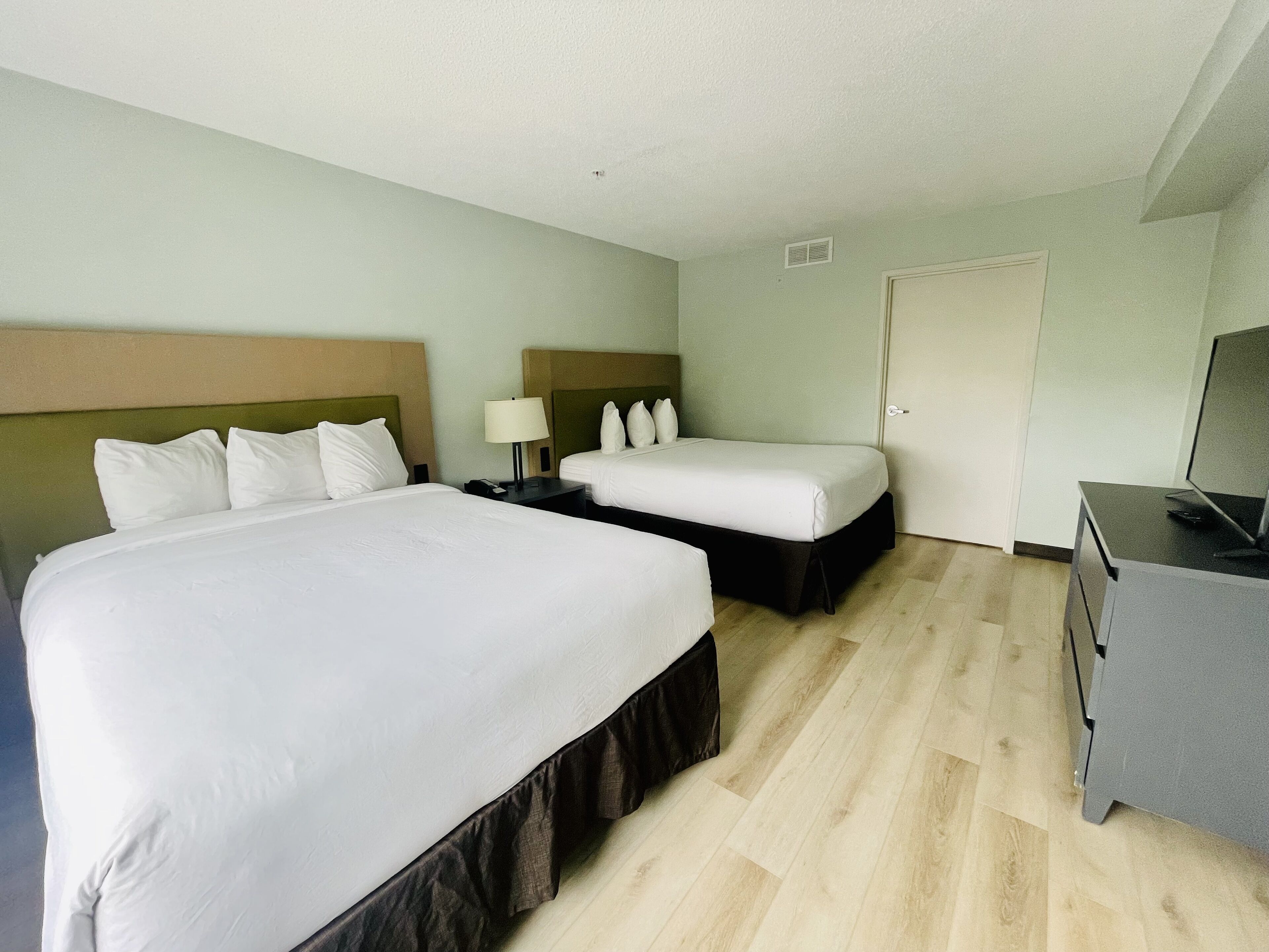 A hotel room with a large bed, a smaller bed, a desk with a computer, and a door.