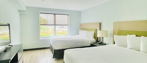 A hotel room with two beds, a desk, and a window.