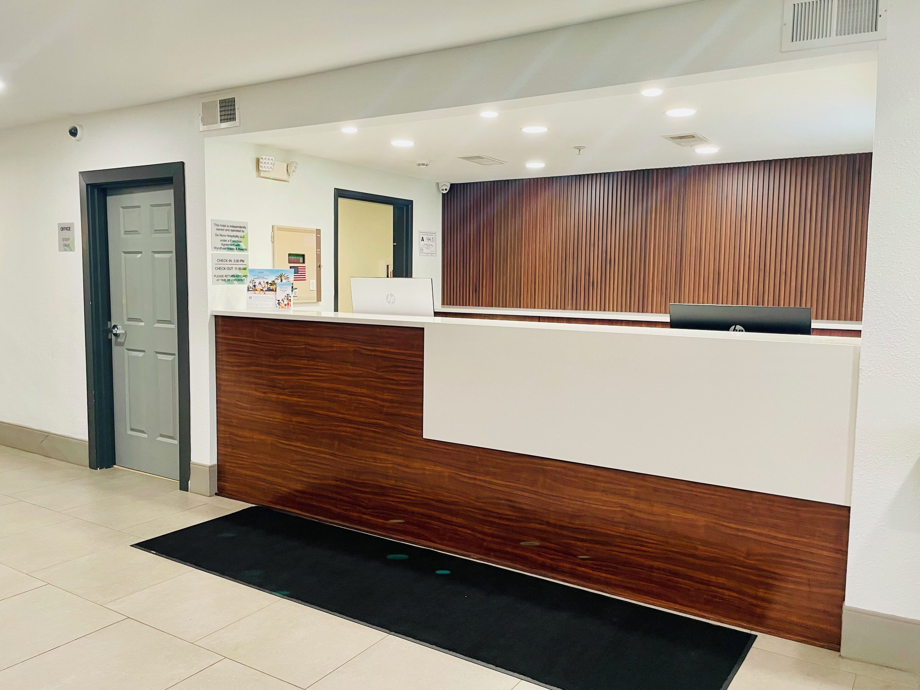 A reception desk with a wooden panel design, a black mat at the entrance, and a sign with check-in times.