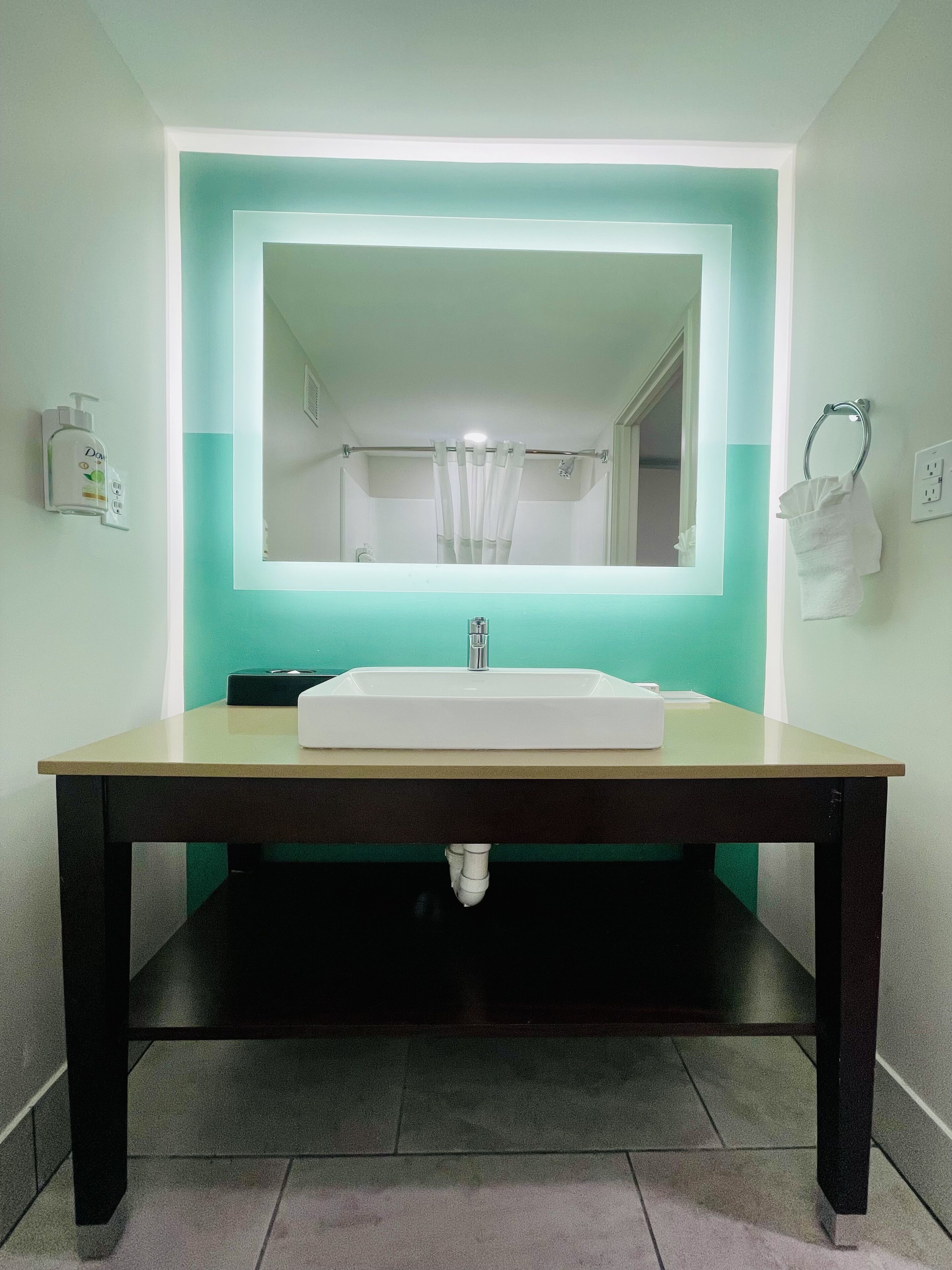A bathroom with a white sink, a mirror, and a lighted wall.