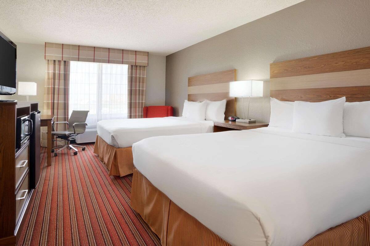 A hotel room with two beds, a desk with a chair, a television, and a window with curtains.