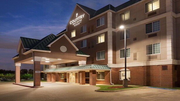 A Country Inn & Suites by Radisson building with a covered entrance, multiple windows, and a parking lot. - Country Inn & Suites by Radisson, DFW Airport South, TX (Irving)