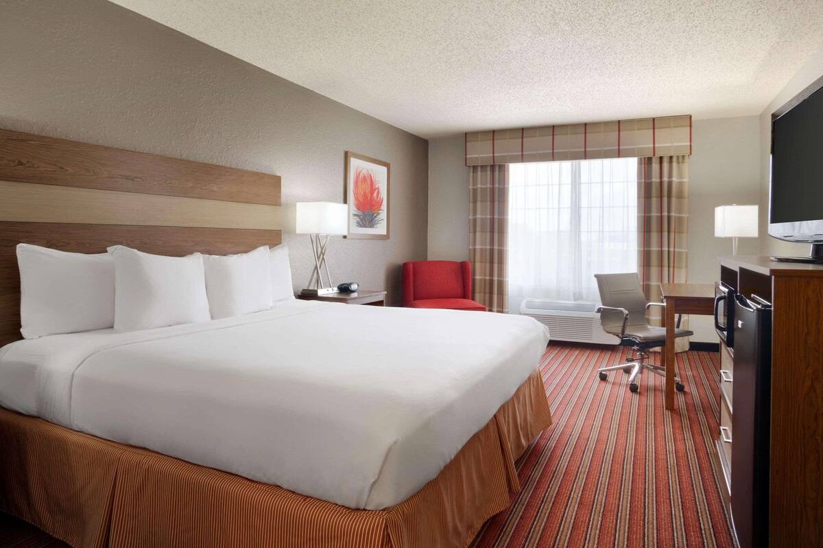 A hotel room with a large bed, a desk with a computer, a chair, a television, and a window with curtains.