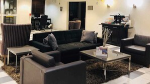 A modern living room with a sofa, armchairs, and a coffee table. There is a desk with a computer and a chair, and a kitchen area with a counter and appliances. - Country Inn & Suites by Radisson, DFW Airport South, TX (Irving)