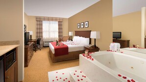 A hotel room with a large bed, a sitting area with a desk, a television, a bathroom with a bathtub, and a minibar. - Country Inn & Suites by Radisson, Houston Intercontinental Airport East, TX (Humble)