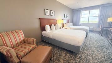 Ein Hotelzimmer mit einem gestreiften Sofa, zwei Betten, einem Schreibtisch und einem Fenster mit Vorhängen.