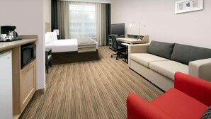 A hotel room with a bed, a desk with a computer, a red chair, a sofa, and a microwave. - Country Inn & Suites by Radisson, Houston Intercontinental Airport East, TX (Humble)