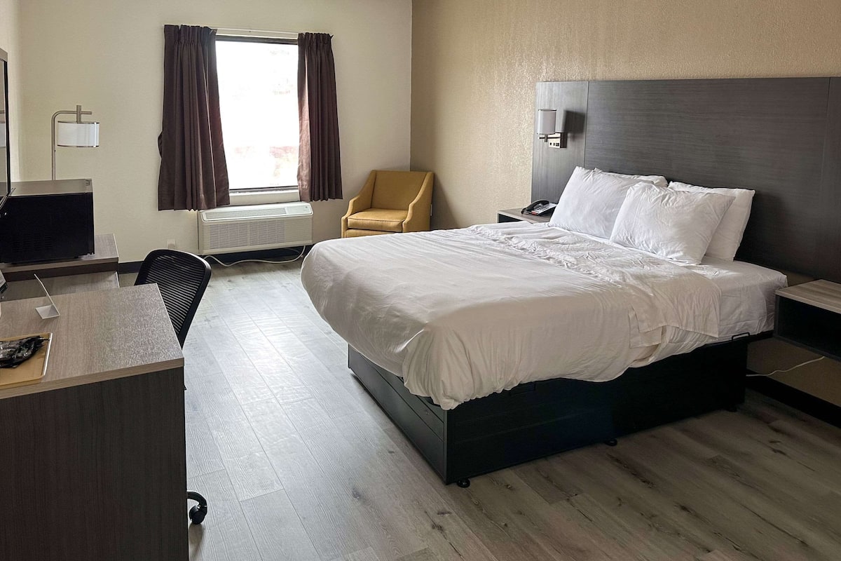 Une chambre d’hôtel avec un lit, un bureau, une chaise et une fenêtre avec des rideaux.