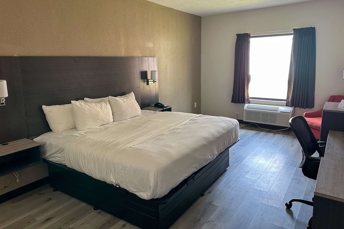 Une chambre d’hôtel avec un grand lit, un bureau avec une chaise, un appareil de climatisation et une fenêtre avec des rideaux.