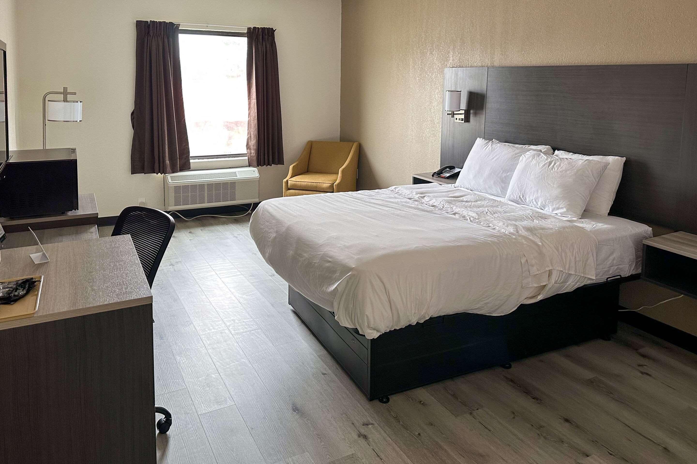 Habitación de hotel con cama, escritorio, silla y ventana con cortinas.